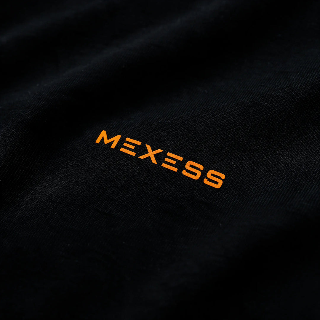 Close-up of the small orange MEXESS wordmark on the chest of the black t-shirt