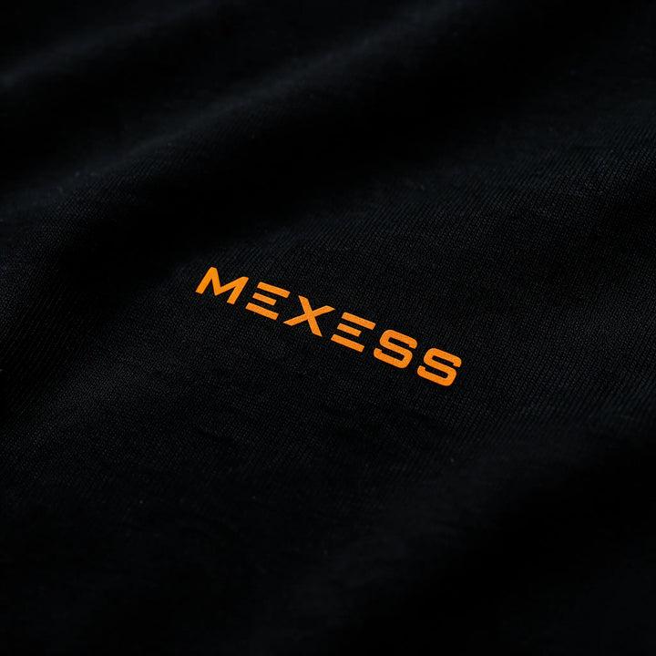 Close-up of the small orange MEXESS wordmark on the chest of the black t-shirt
