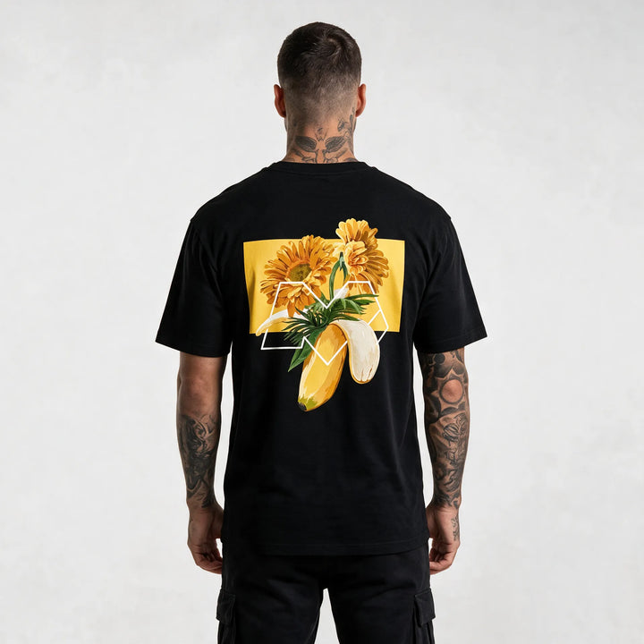 Back of a black banana t-shirt with orange gerberas, palm leaves and a white M outline on a yellow block