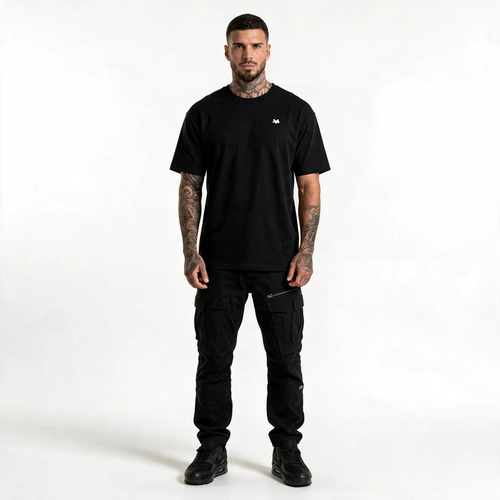 Full-length front view of a man in a black t-shirt with a small chest logo and black trousers
