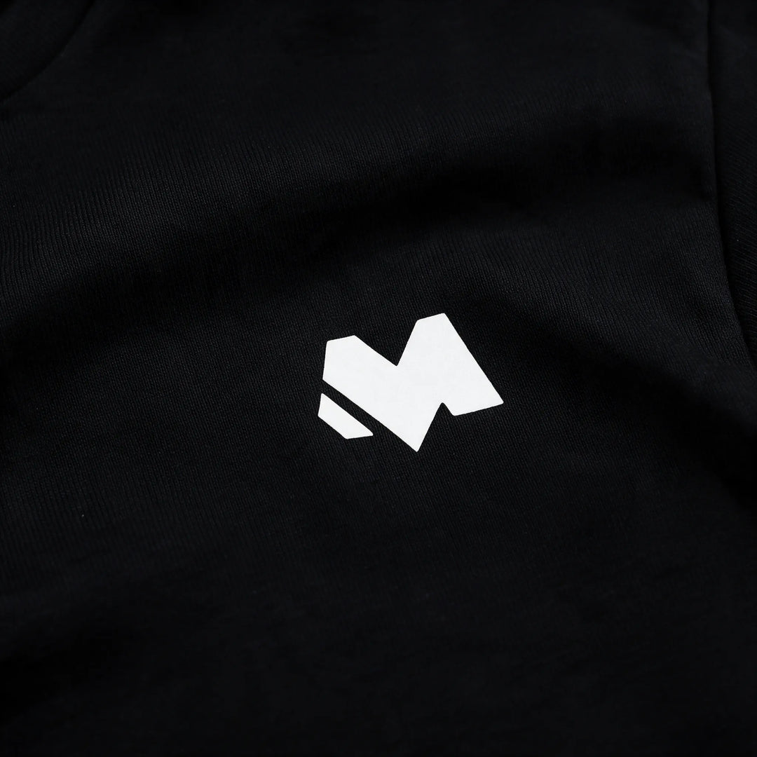 Close-up of the small white MEXESS logo on the chest of a black organic cotton t-shirt