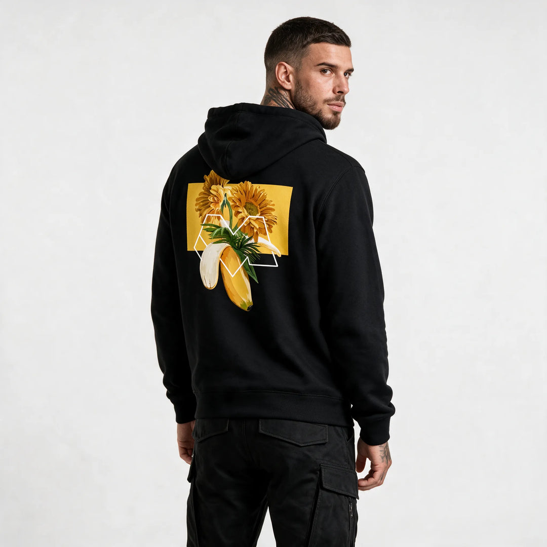 Man in a black flower hoodie in organic cotton, looking over his shoulder to show the gerbera and banana back print
