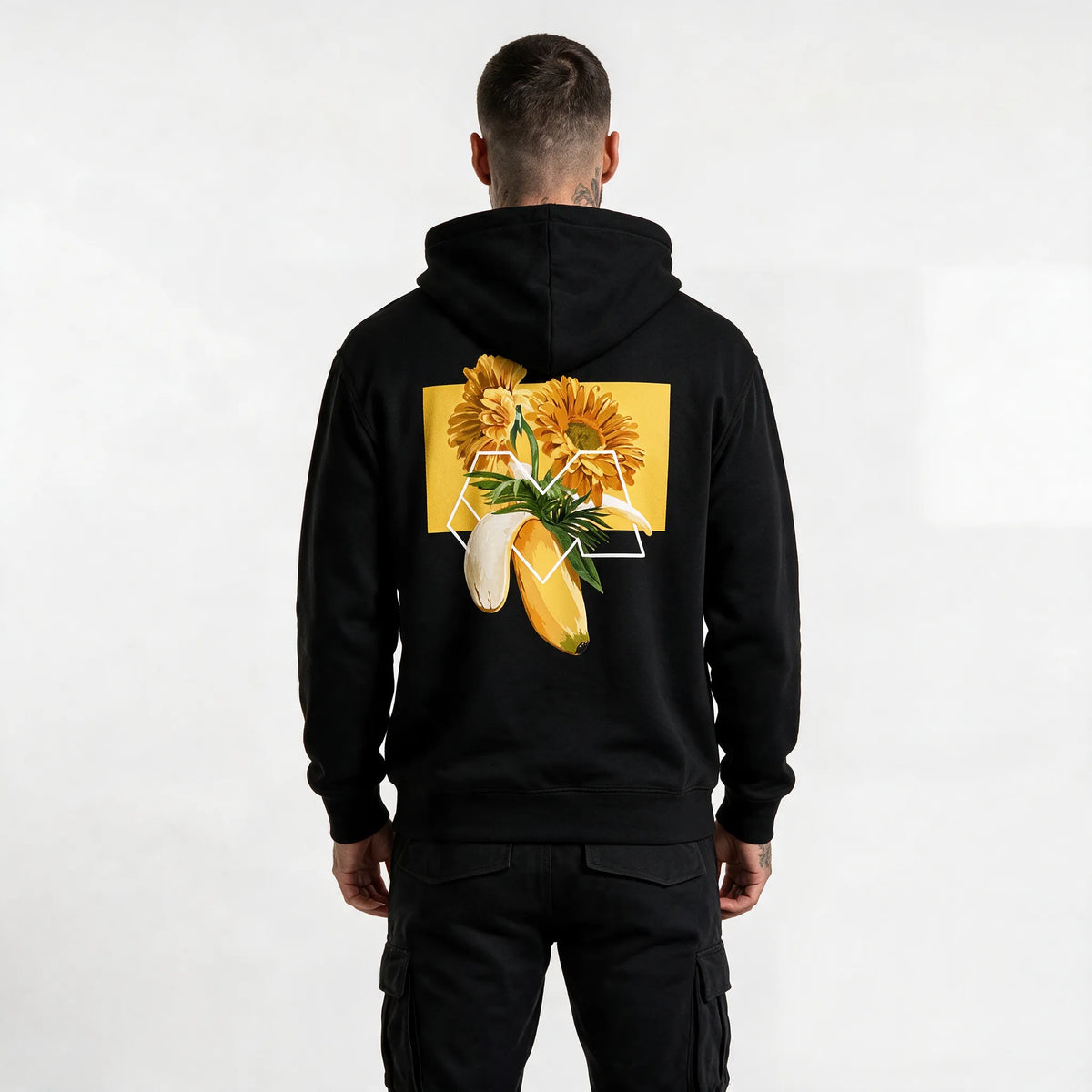 Back of a black banana hoodie with orange gerberas, palm leaves and a white M outline on a yellow block