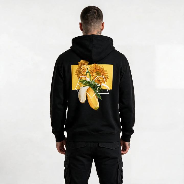 Back of a black banana hoodie with orange gerberas, palm leaves and a white M outline on a yellow block