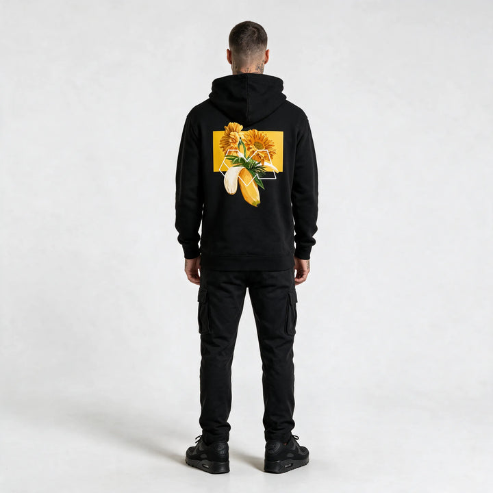Full-length back view of a black hoodie with a gerbera and banana graphic print