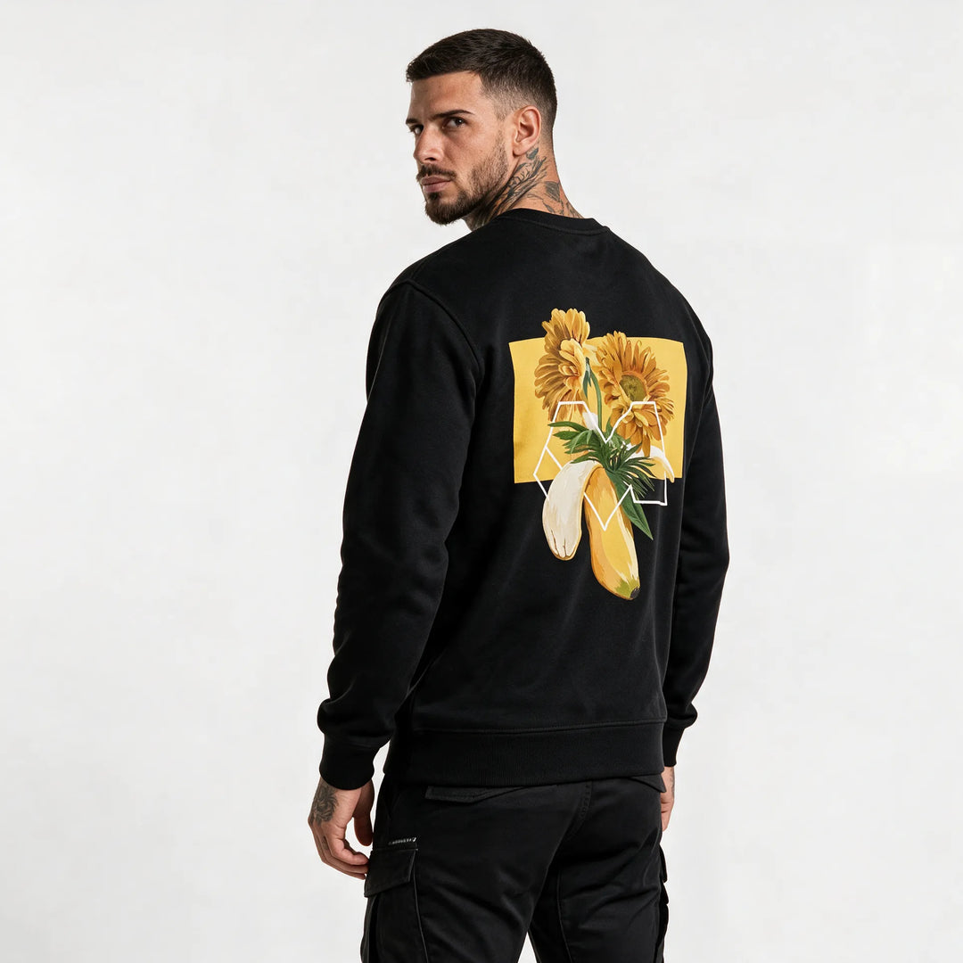 Man wearing a black flower sweatshirt in organic cotton with an orange gerbera and banana back print, seen from behind
