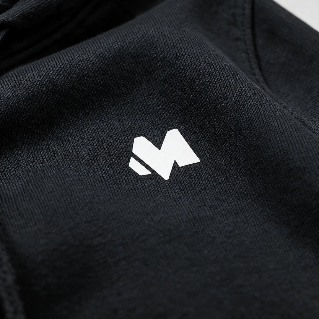 Close-up of the small white MEXESS logo on the chest of a black brushed cotton hoodie