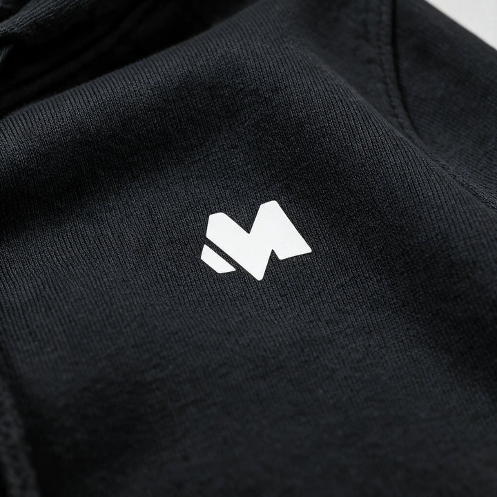 Close-up of the small white MEXESS logo on the chest of a black brushed cotton hoodie