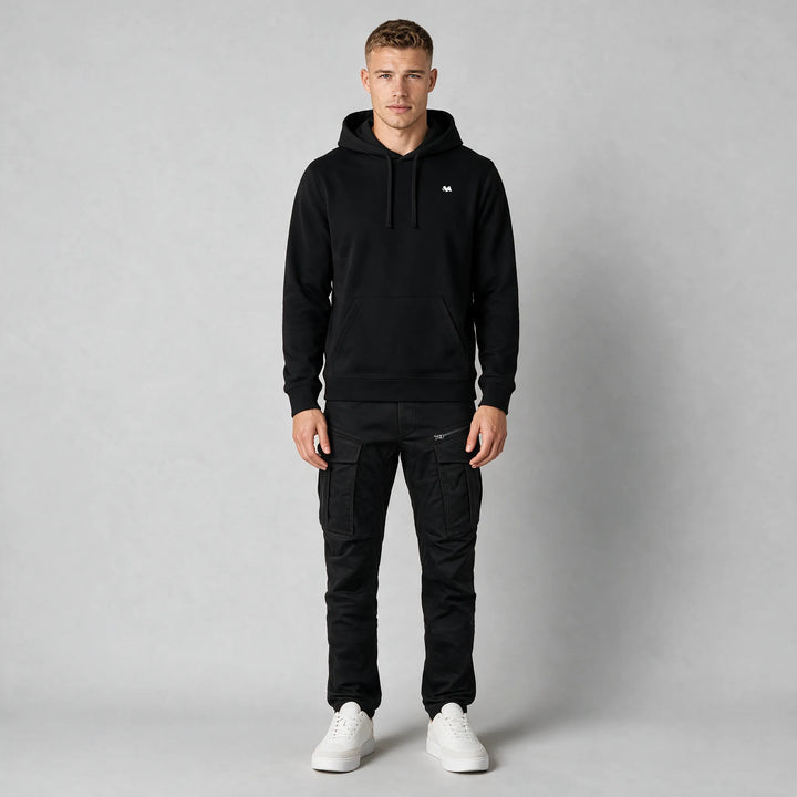 Full-length front view of a black drawstring hoodie worn with black cargo pants and white sneakers