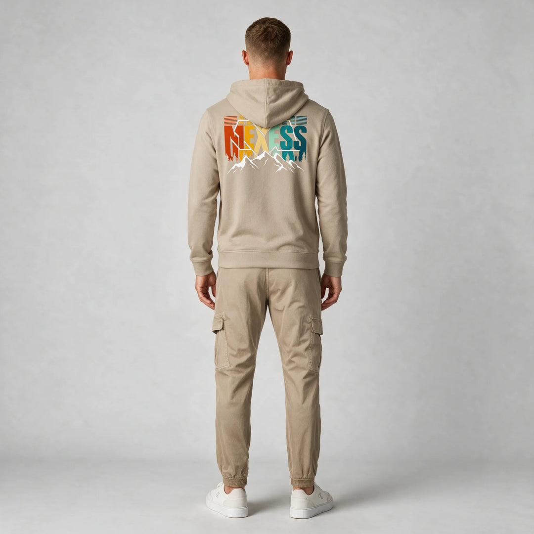 Full-length back view of a man in a beige hoodie with a large MEXESS mountain back print and beige cargo pants