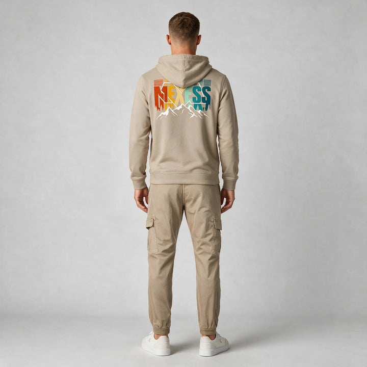 Full-length back view of a man in a beige hoodie with a large MEXESS mountain back print and beige cargo pants