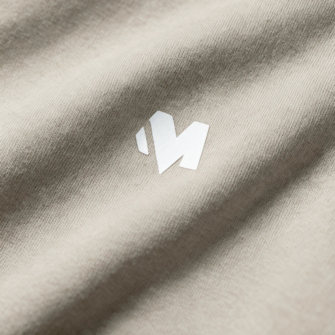 Close-up of the small white MEXESS logo on the chest of a beige brushed cotton hoodie