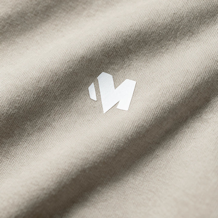 Close-up of the small white MEXESS logo on the chest of a beige brushed cotton hoodie