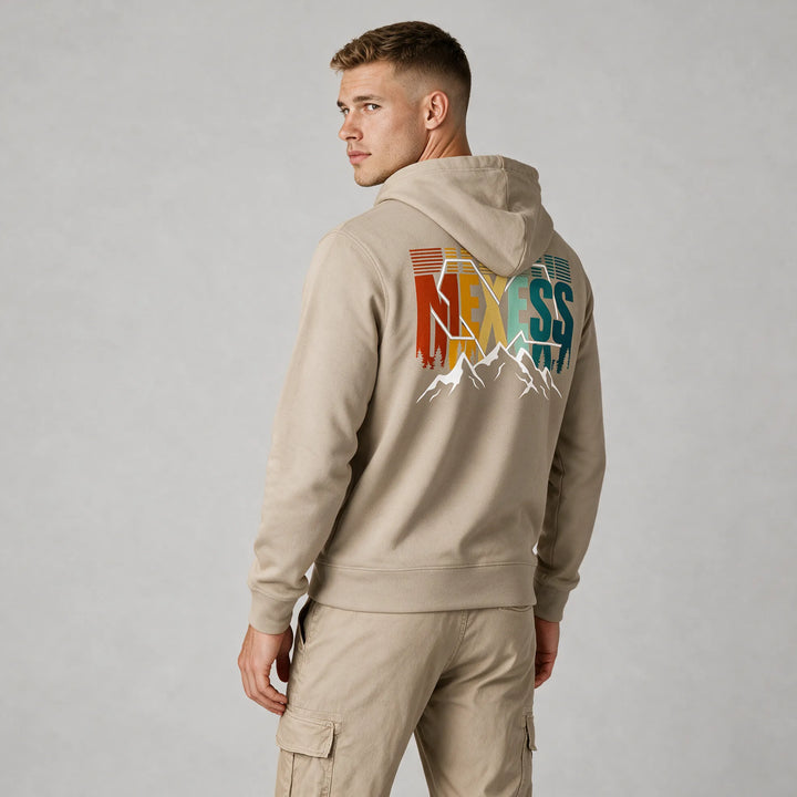 Man wearing a beige mountain hoodie, back view of the rust, yellow and teal MEXESS lettering with white peaks