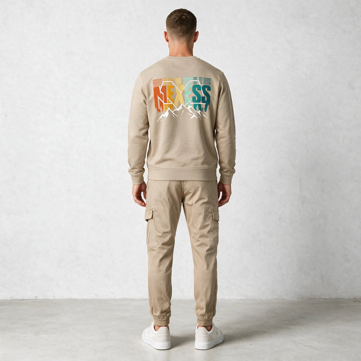 Full-length back view of a man in a beige sweatshirt with a large MEXESS mountain back print and beige cargo pants