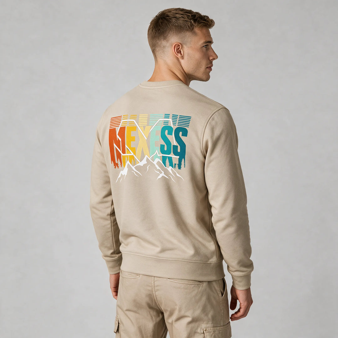 Man wearing a beige mountain sweatshirt, back view of the rust, yellow and teal MEXESS lettering with white peaks