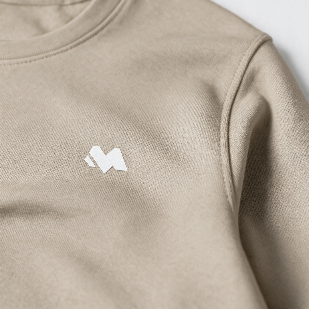 Close-up of the small white MEXESS logo on the chest of a beige brushed cotton sweatshirt