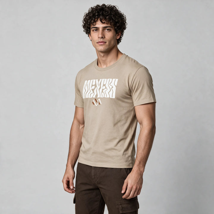 Man in a beige graphic t-shirt with wavy MEXESS lettering and a small logo mark, three-quarter front view