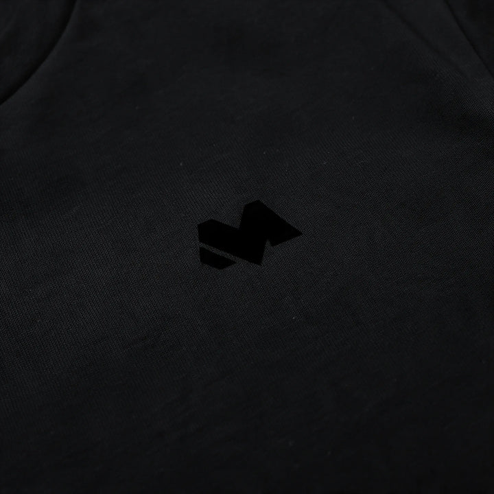 Close-up of the small tonal M logo on the left chest of the black t-shirt