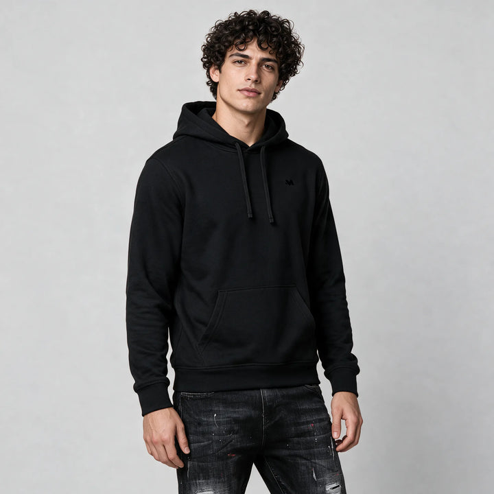 Three-quarter front view of the black organic cotton hoodie with a small tonal M logo on the chest