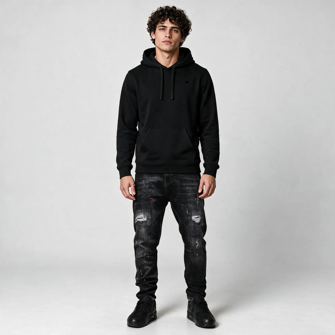 Full-length front view of the black hoodie with a front pocket, worn with dark jeans