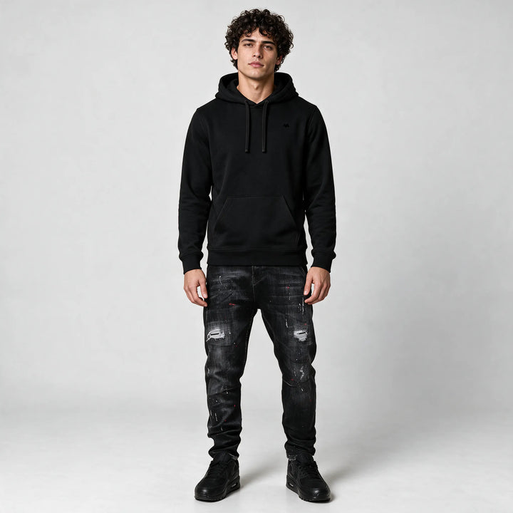 Full-length front view of the black hoodie with a front pocket, worn with dark jeans