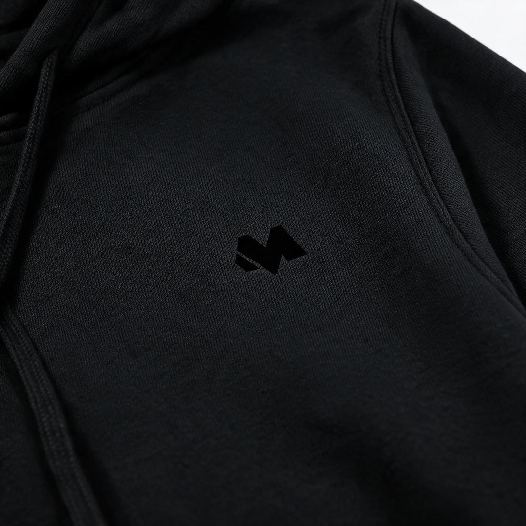 Close view of the small tonal M logo on the chest of the black hoodie
