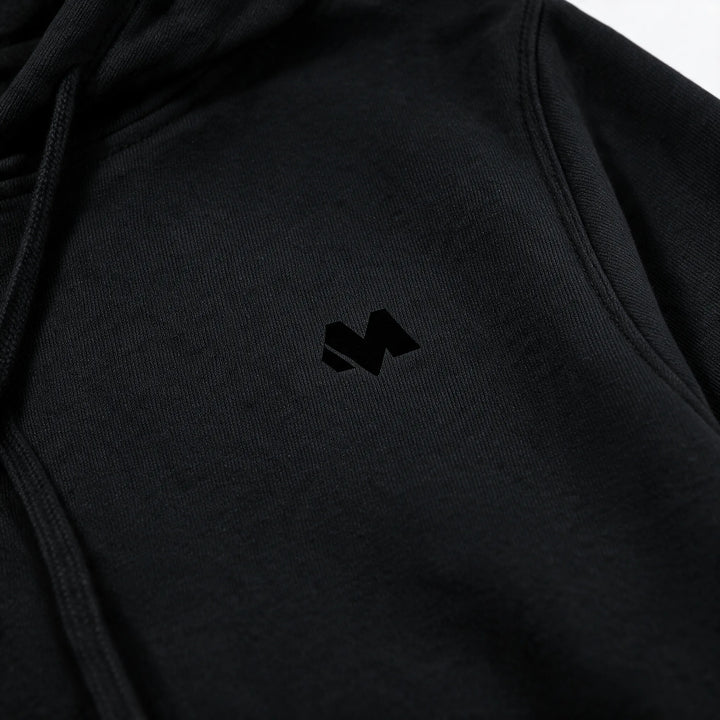 Close view of the small tonal M logo on the chest of the black hoodie