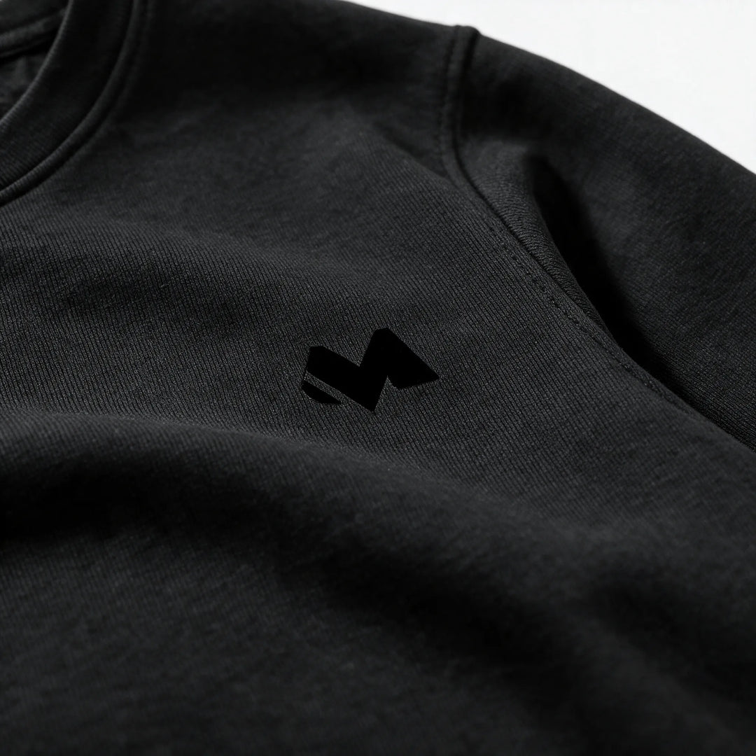 Close-up of the small tonal M logo on the left chest of the black sweatshirt