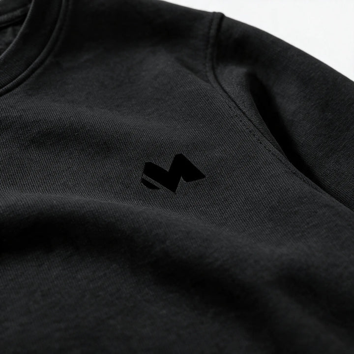 Close-up of the small tonal M logo on the left chest of the black sweatshirt