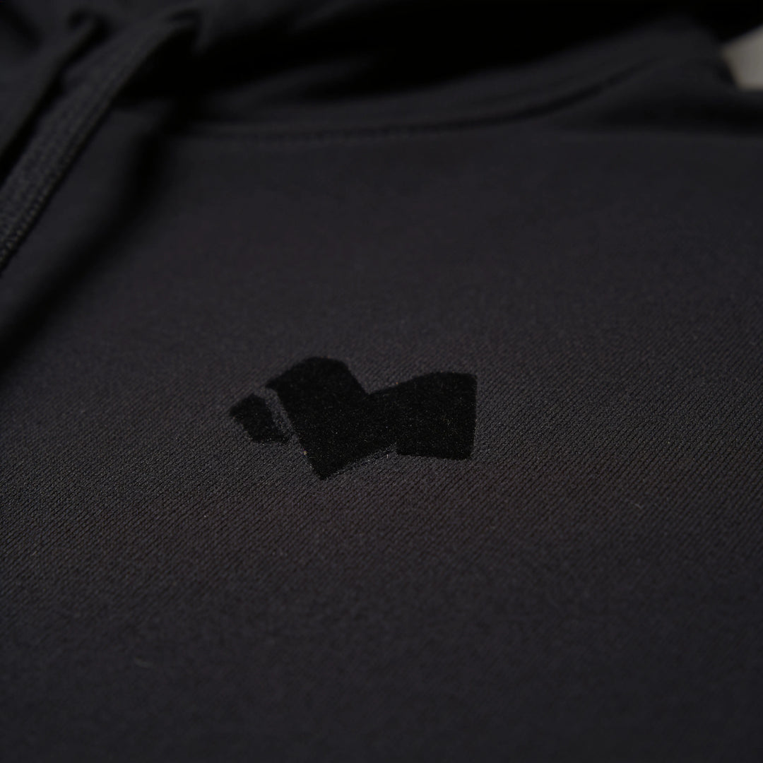 Close-up of the tonal M logo on the chest of the black hoodie