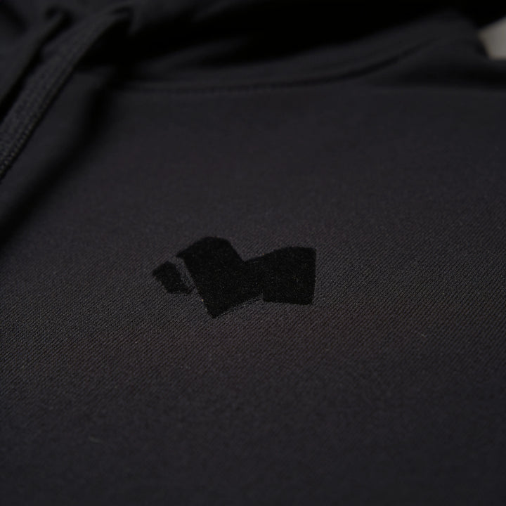 Close-up of the tonal M logo on the chest of the black hoodie